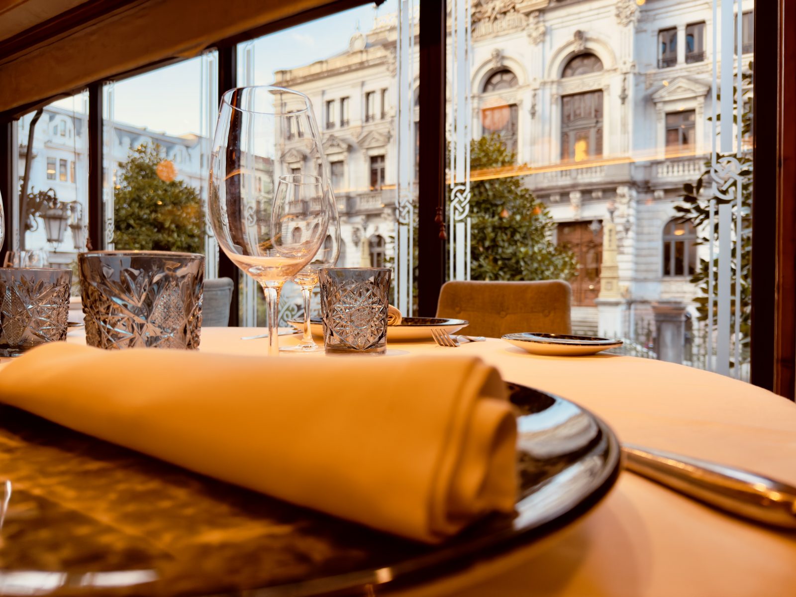 Mesa preparada con vajilla y servilleta naranja con vistas a edificio histórico de Oviedo desde La Corte de Pelayo
